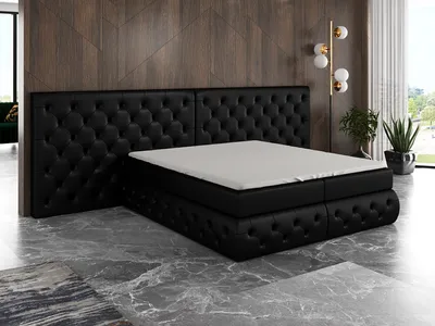 A black tufted boxspring bed with a mattress and topper is shown in a room with a wooden paneled wall and marble floor.