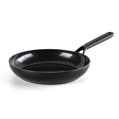A black frying pan with a speckled interior and a black handle is shown against a white background.
