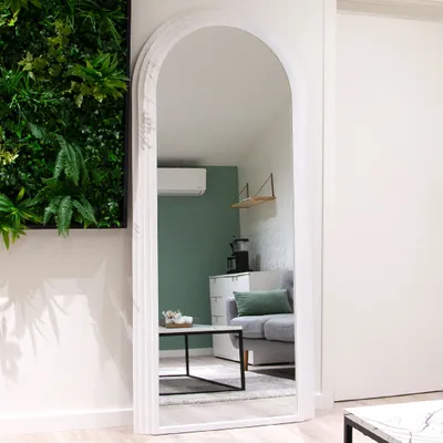 A full-length arched mirror reflects a living room scene with a sofa, coffee table, and a wall-mounted air conditioner.