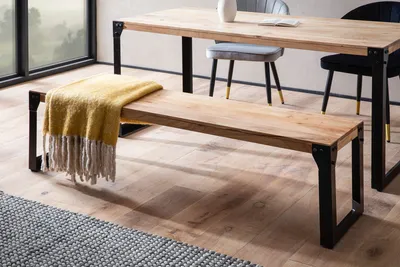 A wooden bench with a yellow throw blanket is placed in front of a dining table in a modern dining room setting.