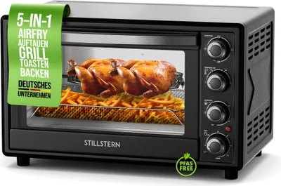 A black Stillstern mini oven with a rotisserie chicken and french fries inside, presented on a white background with a green promotional banner.