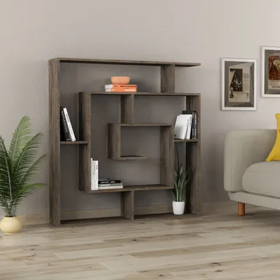 A modern, modular bookshelf is displayed against a plain wall, with a potted plant to the left and a portion of a sofa with a yellow cushion to the right.