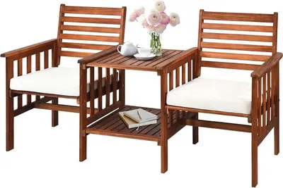 A wooden garden bench with a table and cushions, set against a white background.