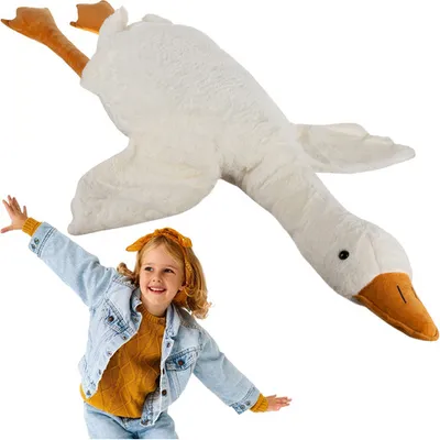 A young girl is happily posing with a large plush goose toy.