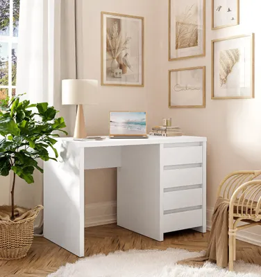 A modern white desk with drawers, a laptop, and a lamp, set in a bright, airy room with artwork on the wall and a plant.