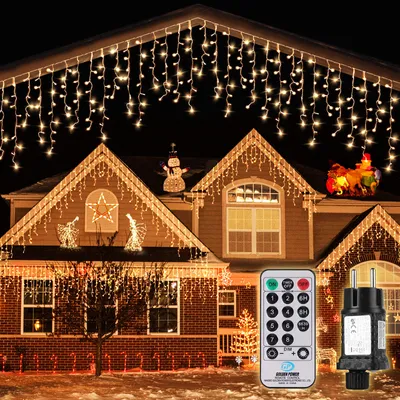 A house decorated with Christmas lights, including icicle lights, angels, a snowman, and candy canes. A remote control and a power adapter are also shown.