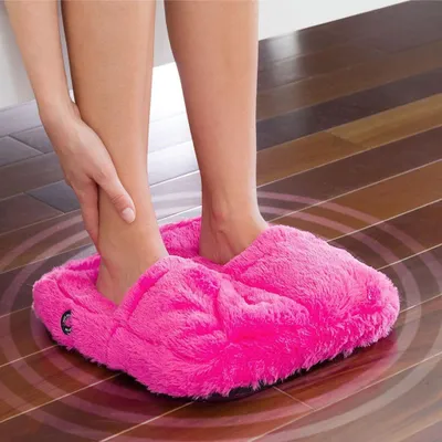 A person's legs and feet are shown wearing pink fluffy slippers while standing on a wooden floor. A hand is touching one of the legs.