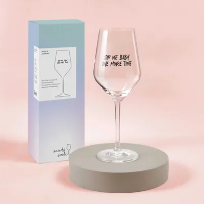 A wine glass with text on it, displayed next to its packaging on a light pink background.