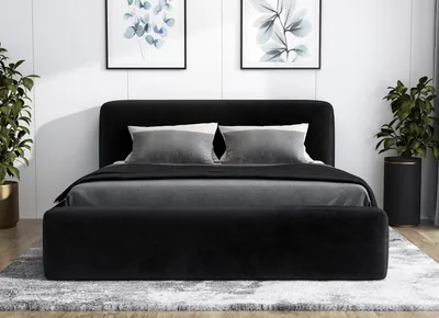 A black upholstered bed frame with gray bedding and pillows, set against a white wall with framed artwork and potted plants.