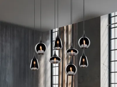 A collection of modern pendant lights hanging from the ceiling in a room with textured walls and large windows.