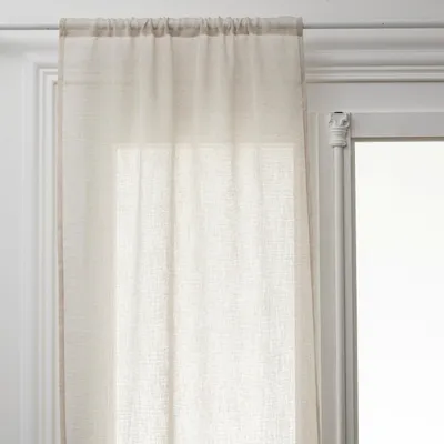 A close-up view of a sheer beige curtain hanging on a white curtain rod in front of a window.