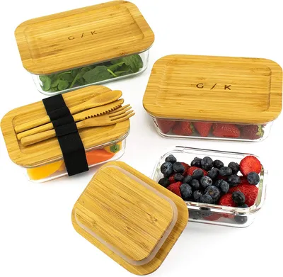 Four glass food storage containers with bamboo lids, filled with various foods like spinach, strawberries, and blueberries.