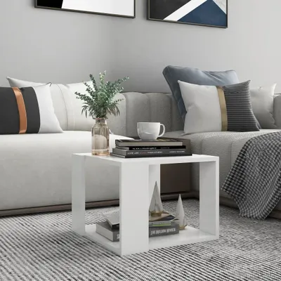 A white side table with books and a vase of greenery on it, placed next to a sofa in a living room.