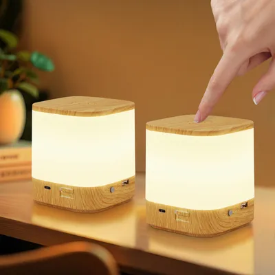 A hand is touching a cube-shaped lamp on a desk, with another identical lamp in the background.
