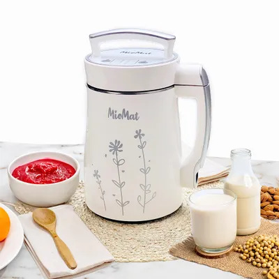 A white MioMat soy milk maker is presented on a marble countertop with various ingredients and finished products, including a bowl of crushed strawberries, a glass of soy milk, a bottle of soy milk, almonds, and soybeans.