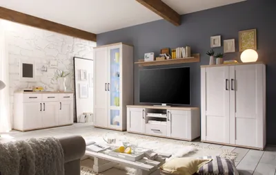 A modern living room with a white stone wall, wooden beams, and a furniture set including a sideboard, display cabinet, and TV unit.