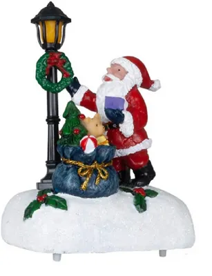 Man sieht den Weihnachtsmann in seinem klassischen roten Anzug mit weißem Bart vor einer Laterne.