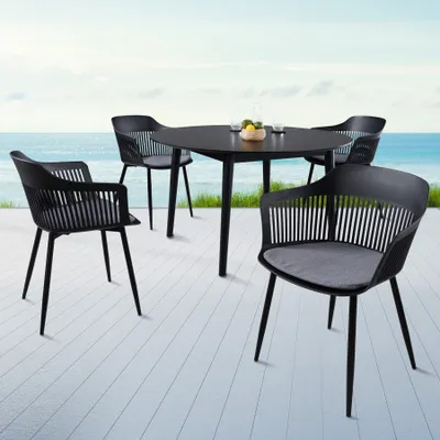 A black outdoor dining set with four chairs and a round table is placed on a white wooden deck overlooking the ocean.
