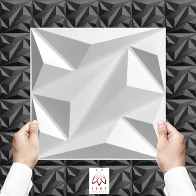 Hands holding a white 3D wall panel in front of a black and gray textured wall.