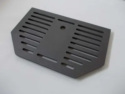 A dark gray, metal grate with horizontal slots and a central circular hole, placed on a white surface.