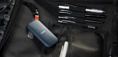 A SanDisk portable SSD is attached to a bag with pens and other items.