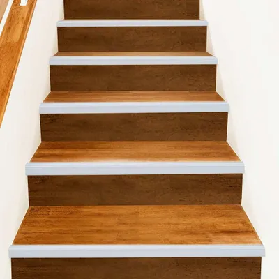 A close-up view of wooden stairs with silver-colored stair nosing strips.