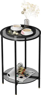 A round, two-tiered side table with a glass top and shelf, holding two cups of coffee, a vase with dried flowers, and a magazine.