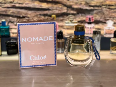 A perfume box and bottle are displayed on a wooden surface with other perfume bottles in the background.