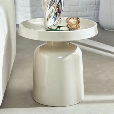 A white side table with decorative items on top, placed next to a sofa.