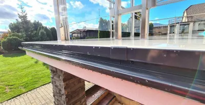 A close-up view of a roof gutter system, with a grassy yard and houses in the background.