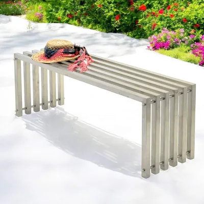 A metal garden bench with a straw hat and scarf on it, placed outdoors on a white surface with a garden in the background.