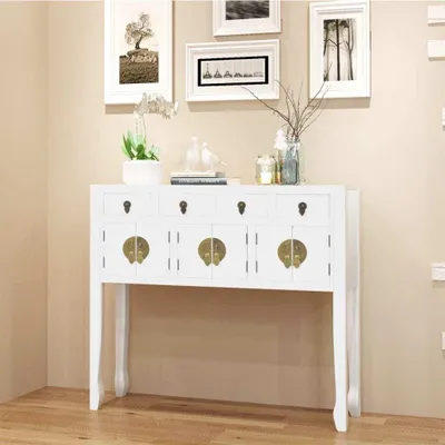 A white console table with brass hardware is displayed against a light beige wall, with framed artwork above.