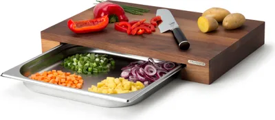A wooden cutting board with a pull-out stainless steel drawer filled with chopped vegetables.