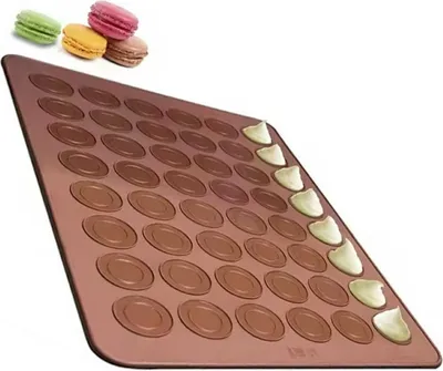 A silicone baking mat with circular indentations for making macarons, with a few macarons shown at the top left and some filling being piped onto the mat.