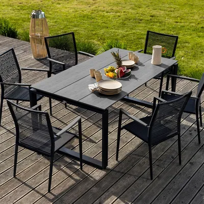 An outdoor dining set on a wooden deck with a grassy background.