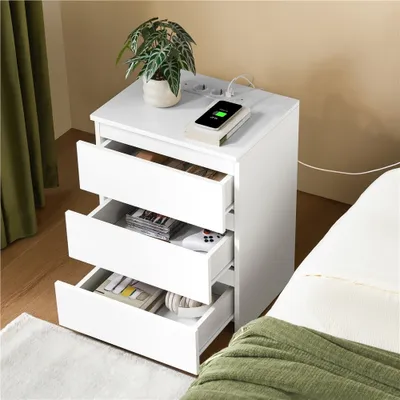 A white nightstand with drawers open, next to a bed with a green blanket.