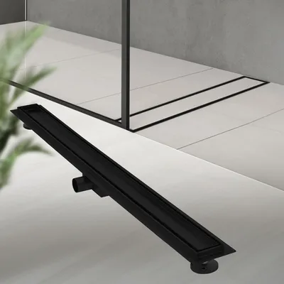 A black linear shower drain is shown on a tiled floor in a modern bathroom setting.