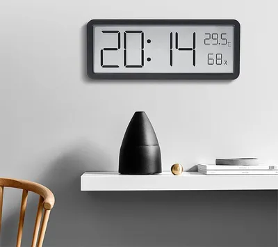 A digital clock and thermometer is mounted on a wall above a white shelf with decorative items.