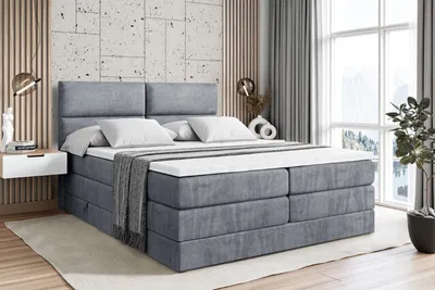A bedroom scene with a large gray boxspring bed as the main focus.