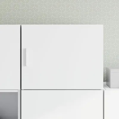 A close-up view of a white cabinet with a minimalist design, set against a patterned wallpaper.