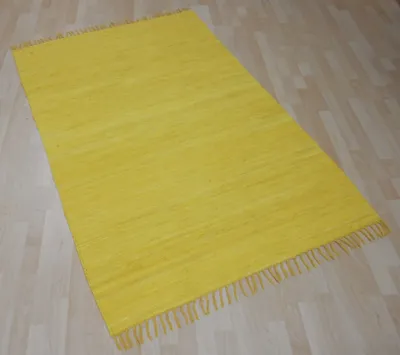 A yellow rug with fringe on a wooden floor.