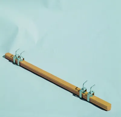 A wooden bar with metal clamps and hooks, laid diagonally on a light blue background.