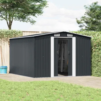 A dark gray metal shed with white trim is shown in a backyard setting, with a wooden deck in the foreground and grass and trees in the background.