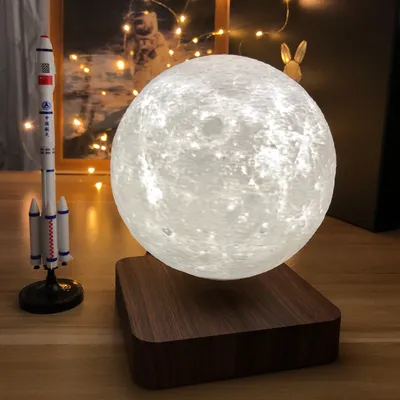 A levitating moon lamp and a rocket model are displayed on a wooden surface, with fairy lights in the background.