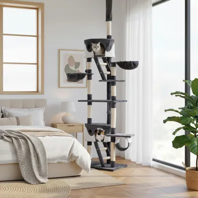A cat tree is set up in a bedroom next to a bed and a window.