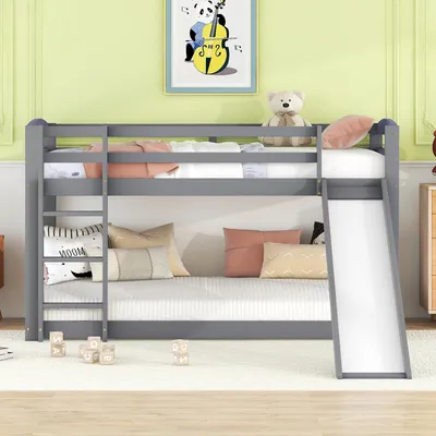A gray bunk bed with a slide and ladder, decorated with pillows and a teddy bear, in a child's room.