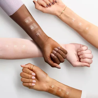 Multiple arms with different skin tones displaying swatches of makeup.