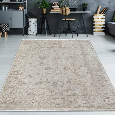 A vintage-style beige rug is placed on a light gray floor in a modern room with a desk and shelving unit in the background.