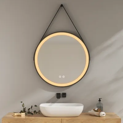 A round LED mirror with a black frame hangs above a white sink on a wooden vanity.