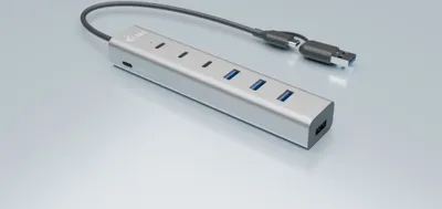 A silver USB hub with multiple ports and a connected cable is shown on a reflective light gray surface.